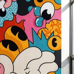 May include: A colorful, abstract rug with a cartoonish design. The rug features a variety of shapes and colors, including pink, blue, orange, and white. The design includes large eyes, bubbles, and other playful elements. The rug is rectangular and appears to be made of a soft material.