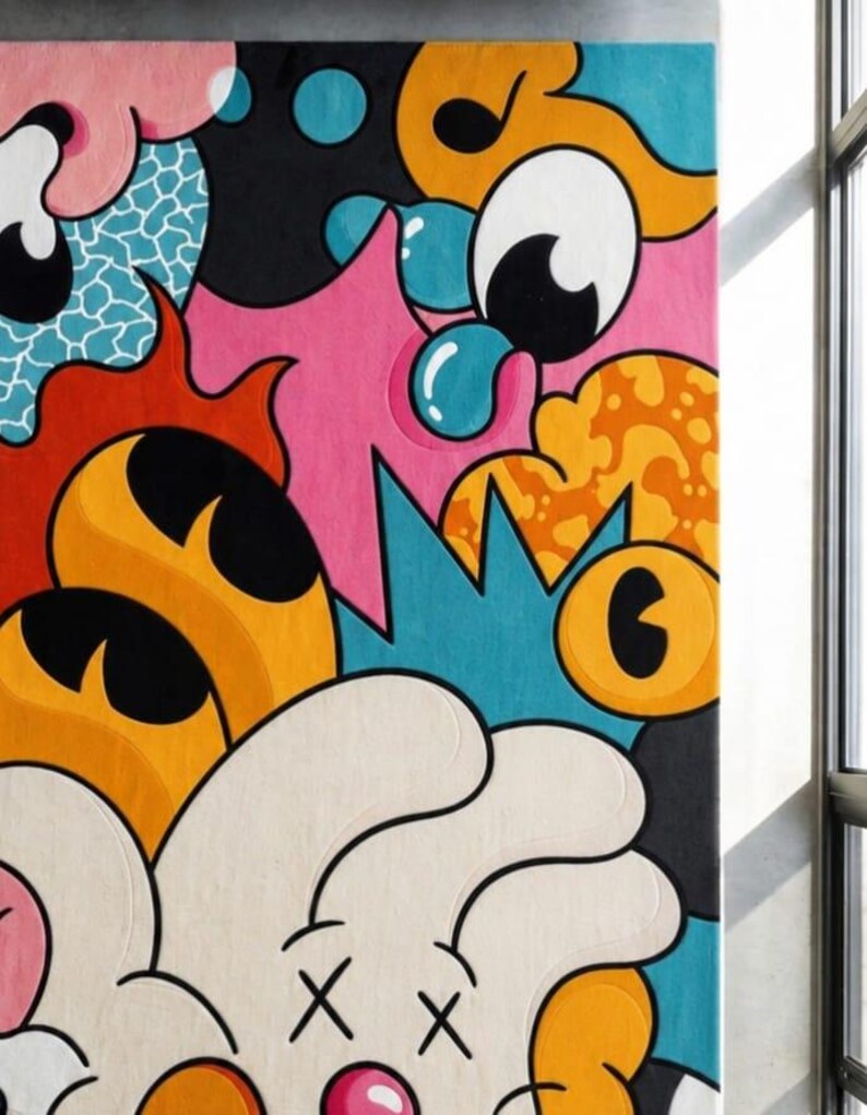 May include: A colorful, abstract rug with a cartoonish design. The rug features a variety of shapes and colors, including pink, blue, orange, and white. The design includes large eyes, bubbles, and other playful elements. The rug is rectangular and appears to be made of a soft material.