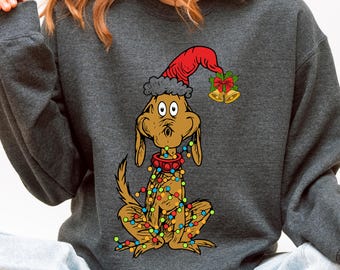 May include: Dark gray sweatshirt featuring a cartoon dog wearing a red Santa hat and a red collar. The dog is adorned with colorful Christmas lights. Gold bells with a red bow are on the right side of the dog's head.