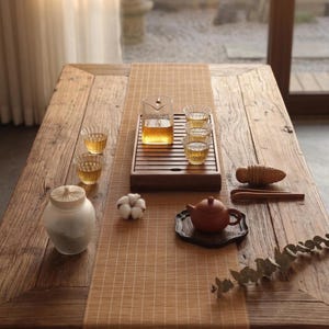 May include: A tea set featuring a glass pitcher, three small fluted glass cups, a brown clay teapot on a dark coaster, a frosted glass jar with a wooden lid, a cotton boll, wooden tongs, and a wooden tool on a rectangular wooden tea tray.