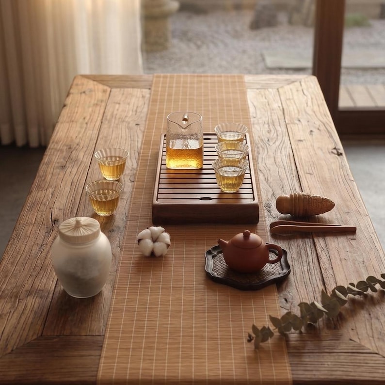 May include: A tea set featuring a glass pitcher, three small fluted glass cups, a brown clay teapot on a dark coaster, a frosted glass jar with a wooden lid, a cotton boll, wooden tongs, and a wooden tool on a rectangular wooden tea tray.