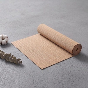 May include: A light brown, rectangular, ribbed mat partially rolled up, accompanied by a small white cotton boll and a dried eucalyptus stem, all featuring a textured surface and neutral, earthy tones for a simple, functional display.