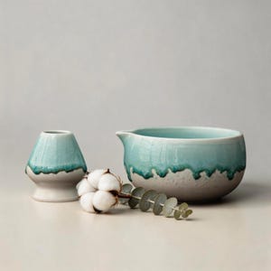 Peut inclure: Un service à thé en céramique avec un glaçage bleu clair et un motif texturé. L'ensemble comprend un petit récipient conique, un bol avec un bec verseur, une branche d'eucalyptus et du coton. L'ensemble est de couleur neutre.