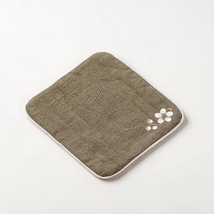 Puede incluir: Un pa&ntilde;o cuadrado verde oliva con borde blanco. Un delicado dise&ntilde;o floral en blanco y dorado adorna la esquina. El pa&ntilde;o tiene un aspecto texturizado, lo que sugiere un material suave y absorbente. Ideal para usar como pa&ntilde;o o art&iacute;culo decorativo.