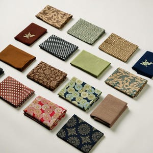 May include: An assortment of folded fabric napkins in various colors and patterns. Designs include floral, geometric, and bird motifs. Colors range from brown, red, and green to blue and tan. The napkins are arranged on a white surface.
