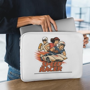 May include: White laptop sleeve featuring a Speed Racer cartoon graphic. The design includes characters and a race car with the text "SPEED RACER" in red. The sleeve is held by a person.