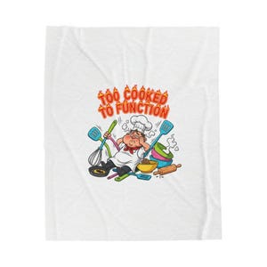 Puede incluir: Una manta blanca con un chef de dibujos animados, exhausto, rodeado de utensilios de cocina. El texto "TOO COOKED TO FUNCTION" se muestra sobre el chef en una fuente llameante, ilustrando un tema humorístico relacionado con la cocina.