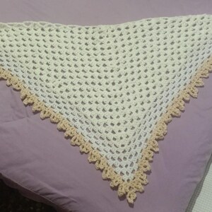 Puede incluir: Un chal triangular de ganchillo color crema con un delicado tejido calado. Los bordes están adornados con un borde festoneado de color beige claro. Este chal hecho a mano es un accesorio acogedor.