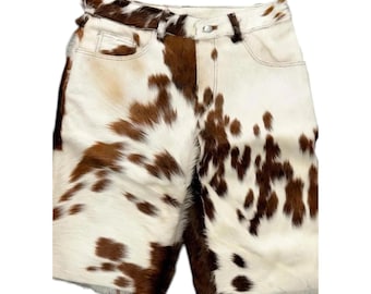May include: Cowhide shorts with a brown and white spotted pattern. The shorts have a classic five-pocket design with a button and zipper closure. The shorts are made of a soft, textured material.
