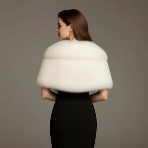 Puede incluir: Un chal de piel sint&eacute;tica blanco drapeado sobre un vestido negro. El chal es de un material suave y esponjoso, y el vestido tiene un dise&ntilde;o simple y elegante. La imagen est&aacute; tomada desde atr&aacute;s, mostrando la forma y textura del chal.