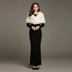 Puede incluir: Una mujer con un vestido largo negro y un chal de piel sint&eacute;tica blanco. El chal est&aacute; drapeado sobre los hombros. El vestido es entallado, con mangas largas y un dobladillo hasta el suelo. El fondo es gris liso.