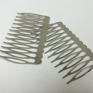May include: Two silver-colored metal hair combs. Each comb has a series of teeth designed to secure hair. The combs are made of a shiny, reflective metal and are positioned on a white surface.