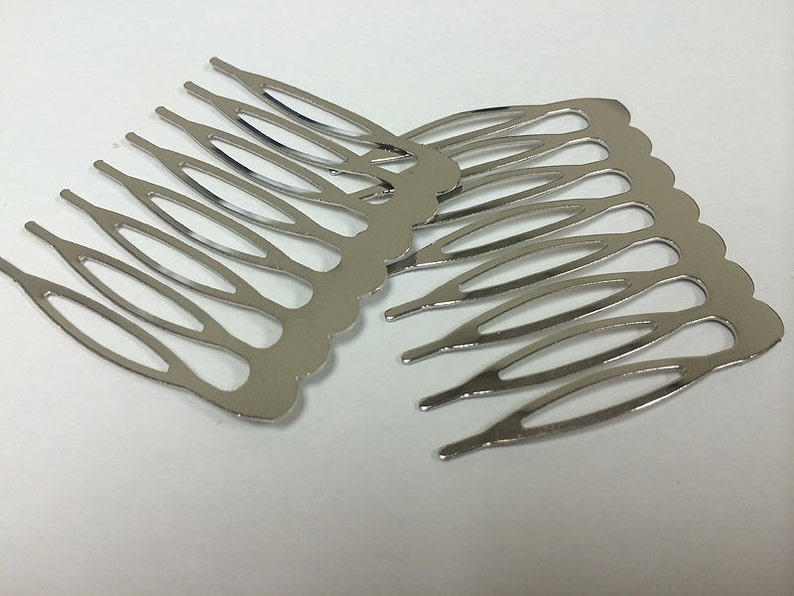 May include: Several silver-colored metal hair combs are arranged on a white surface. Each comb has a scalloped edge and multiple tines. The combs are designed to be inserted into the hair for decorative or functional purposes.