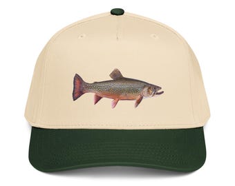 May include: A baseball cap featuring a detailed illustration of a fish. The cap has a cream-colored crown, a dark green brim, and a dark green button on top. The fish is depicted in shades of brown, red, and pink.