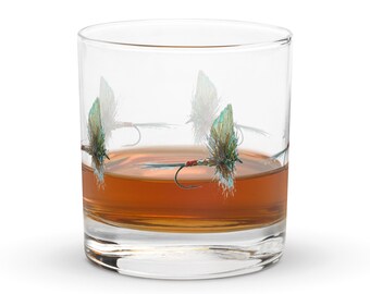 以下が含まれることがあります： 茶色の液体が入った透明なタンブラーグラス。グラスには、緑、茶色、赤の色合いの釣りフライの繰り返し模様が施されています。ウイスキーなどのスピリッツをサーブするのに適しています。