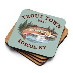 May include: A stack of square coasters with a cork base. The top coaster has a light blue background with a brown trout illustration and the words "Trout Town USA Roscoe, NY" in brown lettering.