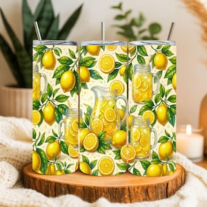 Peut inclure: Trois gobelets en acier inoxydable avec un motif sur le thème du citron. Le motif présente des citrons, des tranches de citron et des feuilles vertes, ainsi qu'une cruche et des bocaux remplis de limonade. Les gobelets ont des pailles argentées et sont posés sur une surface en bois.