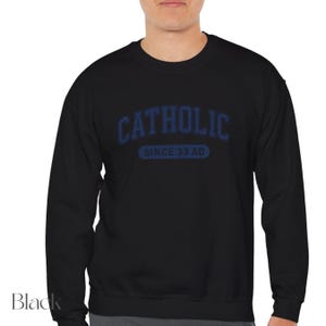 Pu&ograve; includere: Felpa nera girocollo con la scritta "CATHOLIC" in blu, arcuata sul petto. Sotto la scritta, il testo "SINCE 33 AD" in un ovale blu. La felpa &egrave; di colore nero pieno.