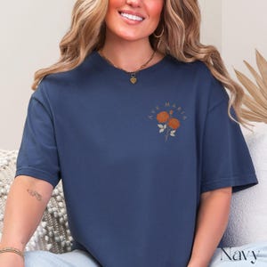 Peut inclure: T-shirt bleu marine avec l'inscription "AVE MARIA" et un motif floral orange. Le t-shirt est de couleur unie et a un col rond. Le mot "Navy" est imprim&eacute; en bas &agrave; droite.