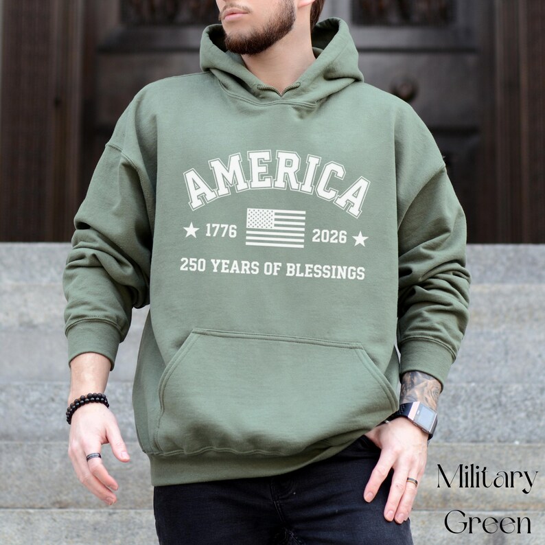 Pu&ograve; includere: Felpa con cappuccio verde militare con la scritta "AMERICA" in bianco. Il design include la bandiera americana, gli anni 1776 e 2026 e la frase "250 YEARS OF BLESSINGS". La felpa ha una tasca frontale.