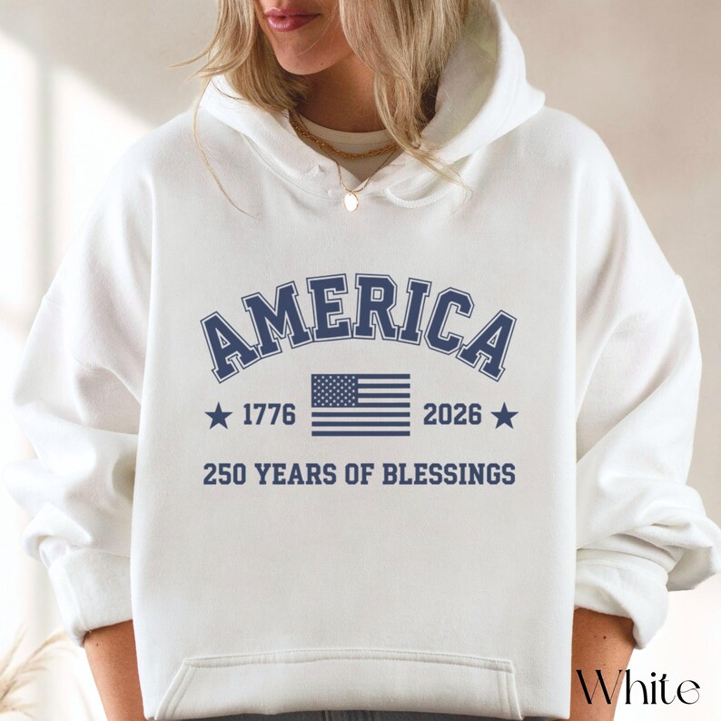 Pu&ograve; includere: Felpa con cappuccio bianca con la scritta "AMERICA" in testo blu navy ad arco. Sotto, la bandiera americana, gli anni 1776 e 2026 e la frase "250 YEARS OF BLESSINGS". La parola "White" si trova nell'angolo in basso a destra.