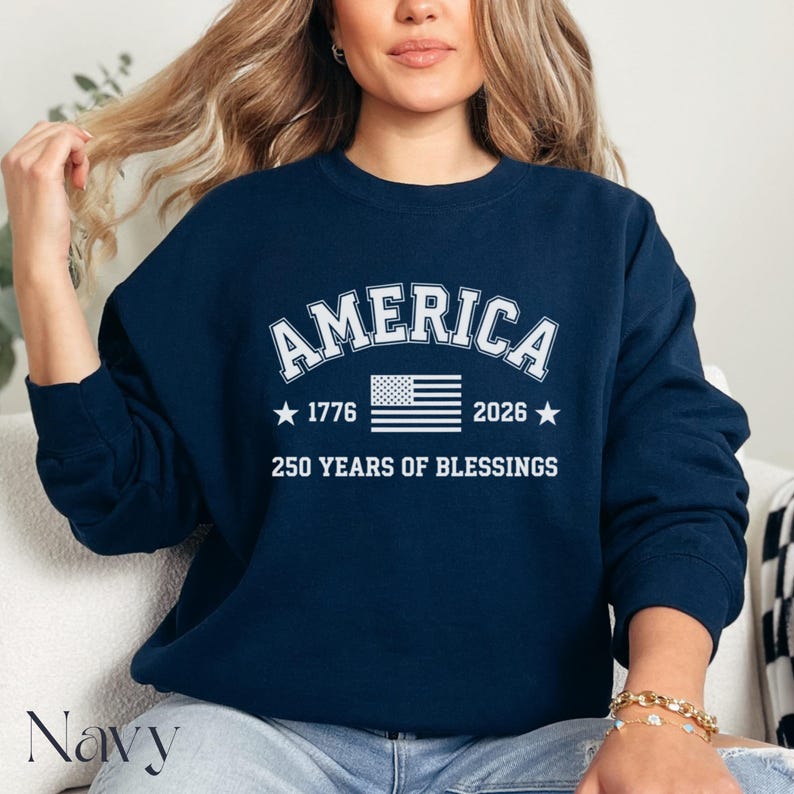 Pu&ograve; includere: Felpa blu navy con la scritta "AMERICA" in lettere bianche. Sotto, una bandiera americana, gli anni 1776 e 2026 e la scritta "250 YEARS OF BLESSINGS".
