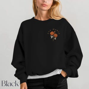 Peut inclure: Sweat-shirt noir avec le texte "AVE MARIA" et un motif floral orange. Le sweat-shirt &agrave; col rond a des manches longues. Le mot "Black" est imprim&eacute; en bas &agrave; gauche de l'image.