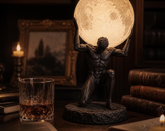 May include: A bronze-colored statue of a kneeling man holding a glowing, spherical lamp resembling the moon. The lamp is on a wooden desk with a glass of amber liquid, books, and a framed picture. The lamp is approximately 12 inches tall.