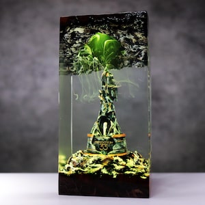 May include: A unique resin sculpture featuring a detailed, green and gold tower with the text "EXPEDITION 33" encased in a clear rectangular block. The top of the block has a dark, textured design, and the sculpture has a smoky, ethereal effect.