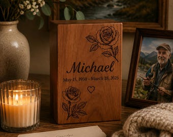 May include: A rectangular wooden cremation urn featuring laser-engraved rose illustrations, the name Michael, and the dates May 15, 1950 - March 28, 2025. The front surface also includes a small engraved heart symbol centered between the two roses.