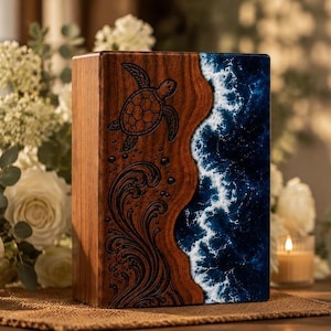 May include: A rectangular wooden urn featuring a laser-engraved sea turtle and swirling wave patterns on the left side, contrasted by a deep blue resin section on the right that mimics the appearance of crashing ocean waves with white foam.