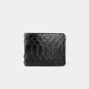 May include: A black wallet with a textured, reptile-skin effect. The wallet is rectangular and has a repeating scale pattern. The material appears to be leather or a similar material. The design is simple and elegant.