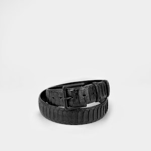 May include: A black belt with a textured pattern and a square buckle. The belt is made of a dark material and is rolled up on a white background. The buckle is also black.