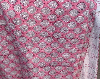 May include: A pink textile with a repeating white teardrop pattern. The fabric has a quilted appearance with visible stitching. A white border with red stitching is visible on the right side. The overall design is a mix of traditional and modern aesthetics.