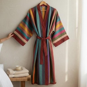 May include: A colorful, striped robe with a matching belt hangs on a wooden hanger. The robe features vertical stripes in shades of red, teal, yellow, and purple. The robe is displayed against a neutral wall, suggesting a cozy, home decor theme.