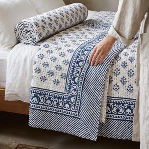 Peut inclure: Une courtepointe en coton blanc ornée d'un motif botanique bleu imprimé au bloc avec des arbres répétitifs, une large bordure décorative à éléments floraux et des bords rayés en diagonale, finie par des lignes de matelassage cousues main.