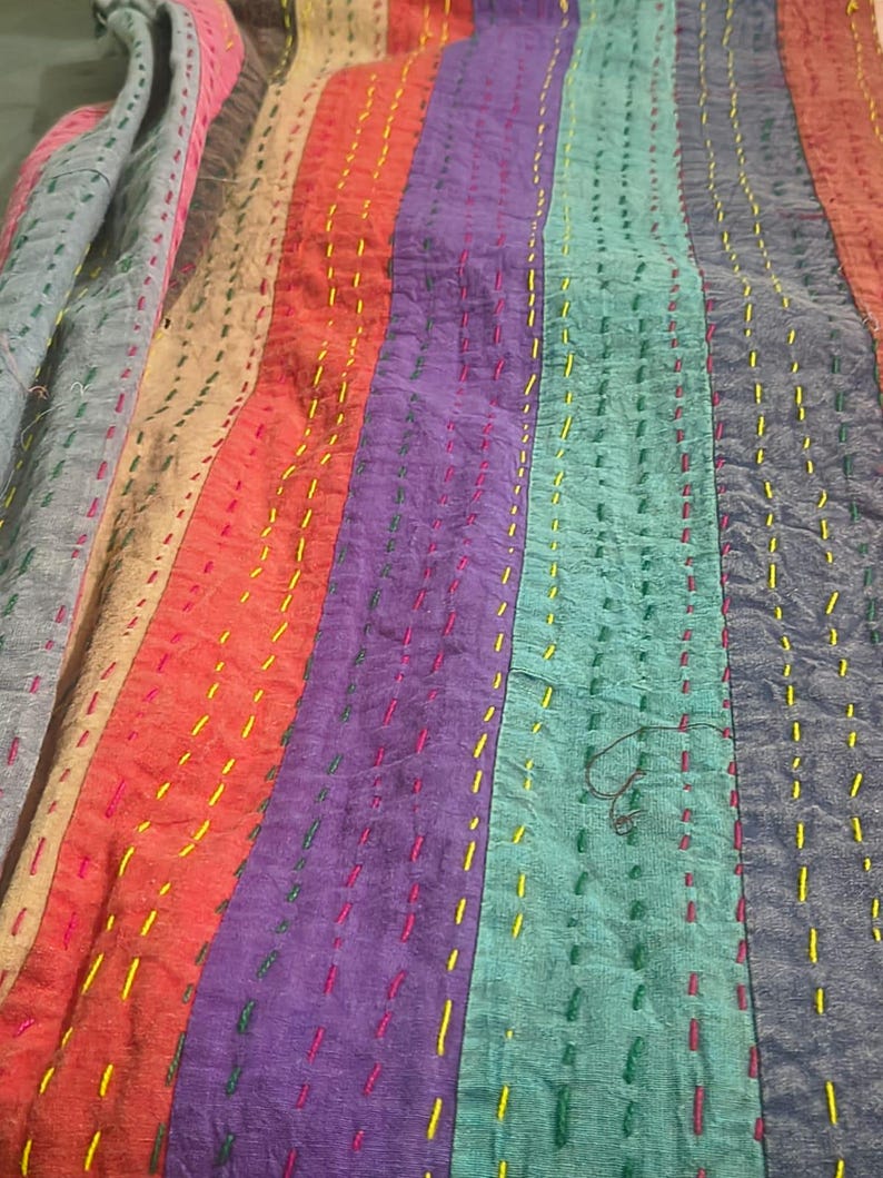 May include: A colorful, striped quilt with vertical bands of various colors, including red, purple, and teal. The quilt is hand-stitched with contrasting thread, adding texture and detail to the design. The overall aesthetic is a blend of rustic and vibrant.