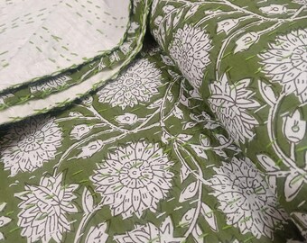 May include: A folded green and white floral quilt. The quilt features a repeating pattern of large white flowers and vines on a green background. The edges are finished with a green border and white stitching.