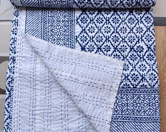 Könnte beinhalten: Eine weiß-marineblaue Steppdecke mit Muster, teilweise aufgerollt. Die Steppdecke hat ein sich wiederholendes Blumen- und geometrisches Design. Die Kanten sind mit einem marineblauen Rand versehen. Die Steppdecke besteht aus einem weichen Material, wahrscheinlich Baumwolle.