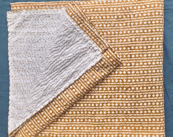 May include: A folded, reversible quilt with a geometric pattern. One side features a mustard yellow and white diamond and stripe design, while the other side is white with a textured, stitched pattern. The quilt is made of soft fabric.