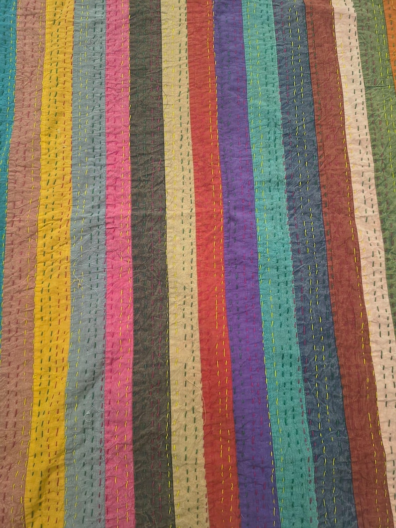 May include: A colorful textile with vertical stripes in various colors, including teal, yellow, red, and purple. The fabric has a textured appearance with visible stitching in a contrasting yellow thread, creating a patchwork effect. The overall design is a vibrant and eye-catching display.