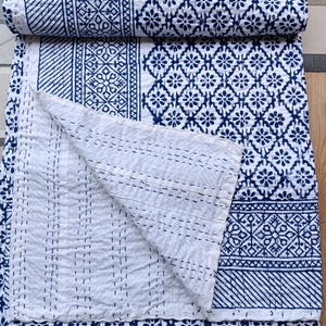 May include: A rolled-up white and navy blue quilt with a floral and geometric pattern. The quilt is made of a soft material and has a stitched design. The quilt is folded over to show the white underside.