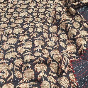 May include: A dark navy blue textile with a repeating floral pattern in beige and red. The fabric is stitched with red and white thread, creating a quilted effect. The design features stylized flowers and leaves.