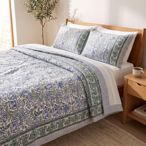 May include: A quilted bedspread and two matching pillow shams featuring a blue and green floral block print pattern on a white background. The bedding set includes a decorative border with a striped edge and a detailed botanical motif throughout.