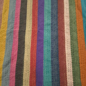 May include: A colorful textile with vertical stripes in various colors, including yellow, pink, red, purple, and teal. The fabric is stitched with yellow thread, creating a textured appearance. The overall design is vibrant and eye-catching.