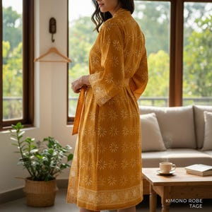 May include: A mustard yellow kimono robe featuring a repeating white starburst pattern and a wide decorative border at the hem. The garment includes long sleeves, a tie-waist belt, and a textured fabric finish, shown from a side profile view.