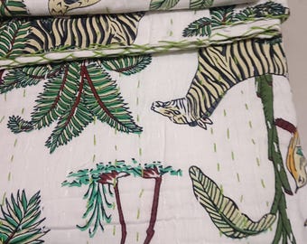 May include: White fabric with a repeating pattern of green leaves, brown tree trunks, and tiger stripes. The fabric is folded, revealing the pattern. The edges are stitched with green thread. The overall theme is a jungle or safari.