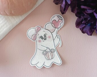 Puede incluir: Una pegatina con temática de Halloween que presenta un fantasma de dibujos animados con un diseño inspirado en Minnie Mouse. El fantasma sostiene una cesta de golosinas con forma de calabaza y un globo rosa con un diseño de telaraña.