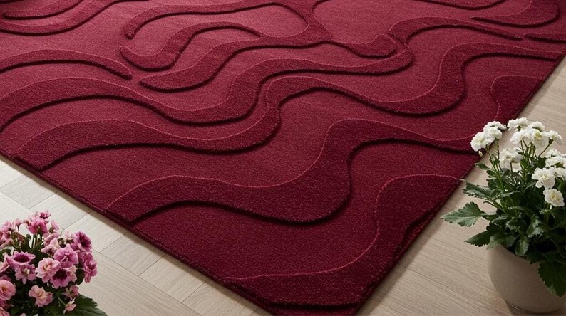 Puede incluir: Una alfombra burdeos con un patr&oacute;n ondulado en relieve. El dise&ntilde;o de la alfombra presenta l&iacute;neas fluidas en diferentes tonos de burdeos, creando un efecto texturizado. La alfombra est&aacute; colocada sobre un suelo de madera clara.