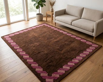 Tappeto marrone cioccolato, in lana trapuntata a mano, con bordo geometrico rosa, ideale per un soggiorno moderno e minimalista, disponibile nelle misure 5x8, 6x9, 8x10 e 9x12.